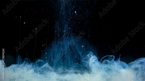 White paint drop mixing in water towards to camera. Ink swirling underwater. Cloud of ink isolated on black background. Abstract smoke explosion effect with particles.