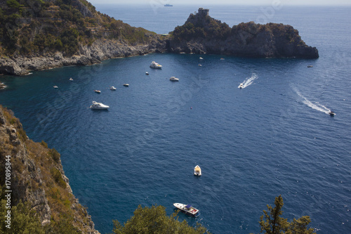 Vista del panorama della costiera Amalfitana tra Positano e Amalfi, in Campania, Italia. La vista del mare e delle barche sottostanti è ostacolata dagli alberi e dalle foglie verdi.