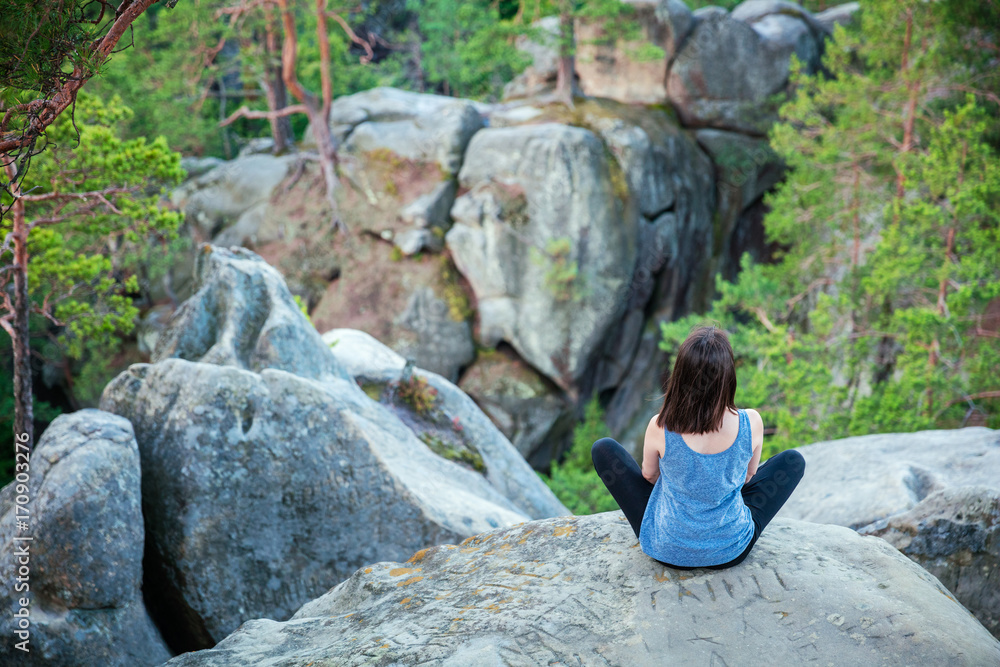 Young girl sitting on top of cliff and watching rocky landscape