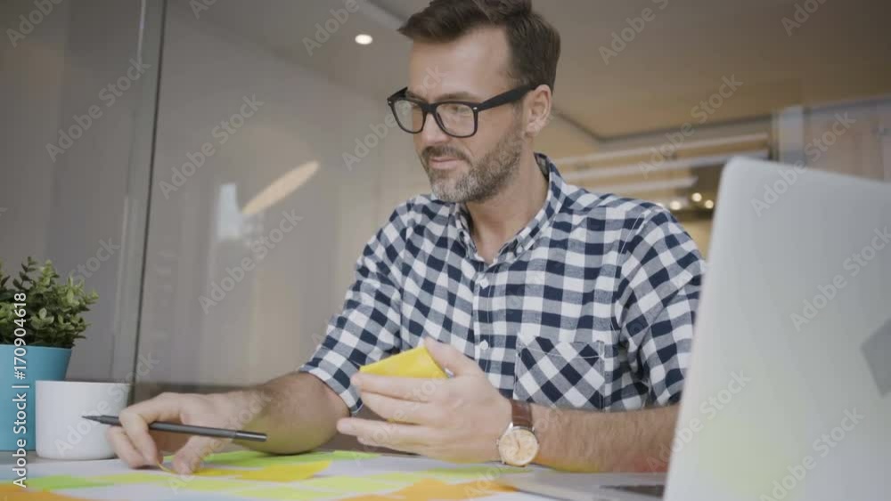 Smiling male creative worker sticking notes to plans and working in home office Smiling male creative worker sticking notes to plans and working in home office