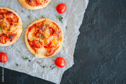 Mini pizzas margheritas on a parchment paper on a black stone background