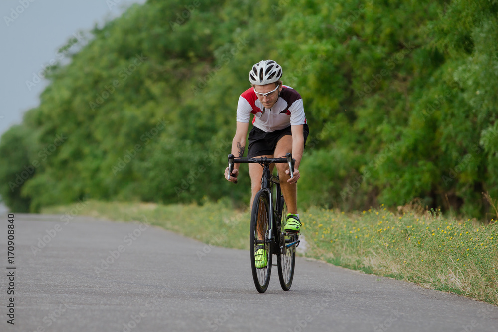 Bicycle racer in helmet and sportswear training alone on empty country road, fields and trees background Bicycle racer in helmet and sportswear training alone on empty country road, fields and trees background
