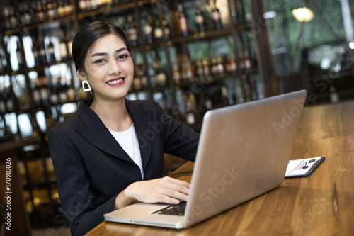 Asian Woman using laptop in restaurant with Attractive Smiling, Woman working Concept