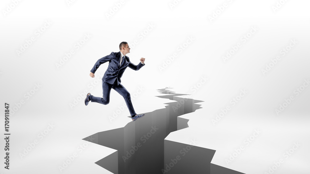 A businessman high-jumps over a long jagged earthquake rift in the ground.