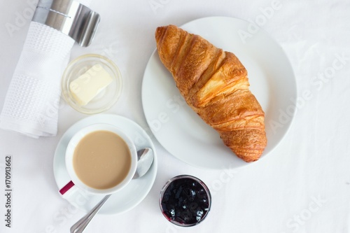 Top down view of croissant served with coffee, butter and blueberry jam