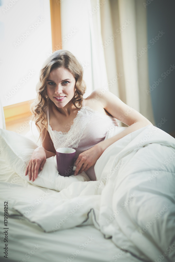 Young woman drinking cup of coffee or tea while lying in bed. Young woman drinking cup of coffee or tea while lying in bed.