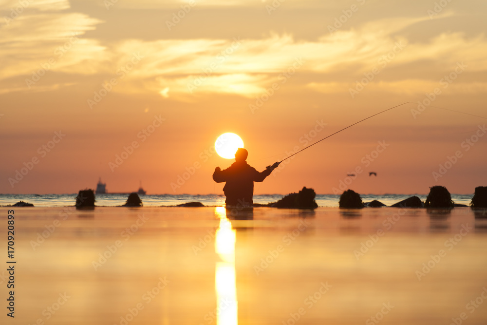 ein Fliegenfischer steht im Morgengrauen am Meer und schwingt die Rute