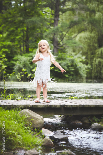 Cheerful little girl standing on wooden bridge