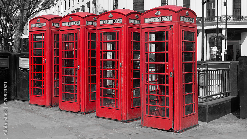 Black and white image with four colour color popped red uk telephone boxes in a line in a london street