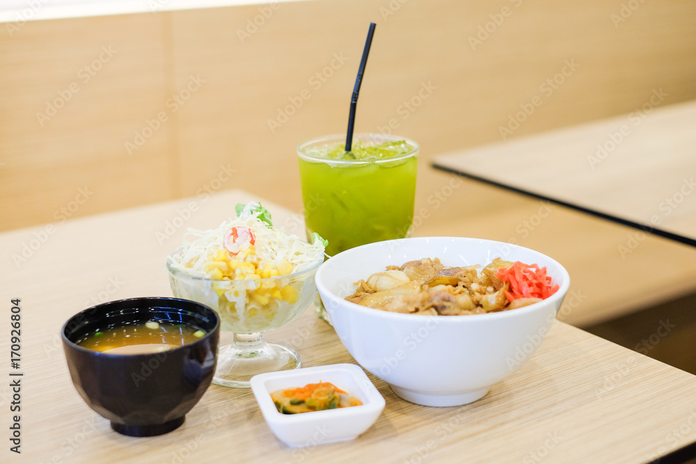The food set consists of rice with grilled pork teriyaki, spring onion & carrot on top white bowl serve with tofu soup (Miso soup), tomato, cabbage & corn salad and green tea - japanese food concept. The food set consists of rice with grilled pork teriyaki, spring onion & carrot on top white bowl serve with tofu soup (Miso soup), tomato, cabbage & corn salad and green tea - japanese food concept.