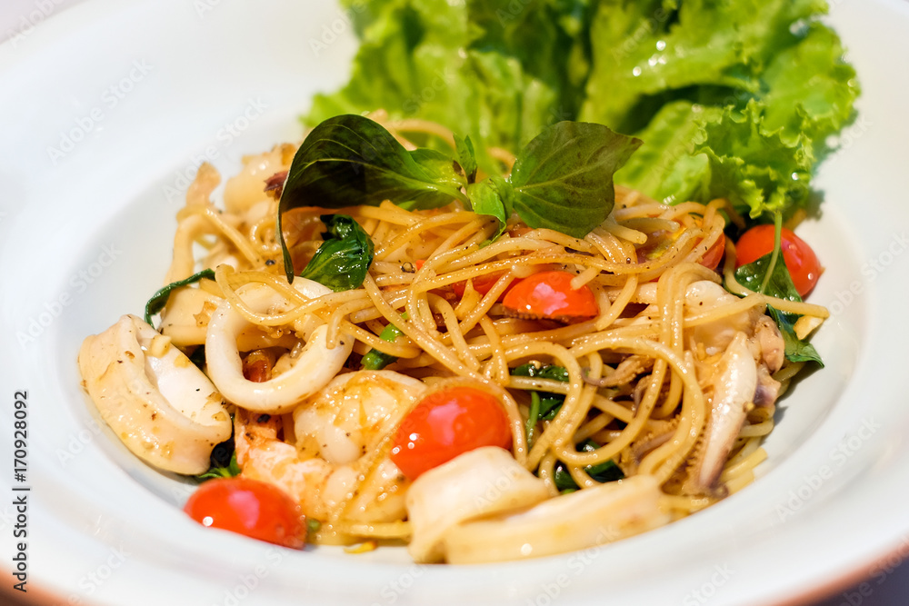 The spaghetti spicy seafood (squid, shrimp) with basil, tomato, black pepper, lettuce and paprika on white dish set on table for food background or texture - homemade food concept. The spaghetti spicy seafood (squid, shrimp) with basil, tomato, black pepper, lettuce and paprika on white dish set on table for food background or texture - homemade food concept.