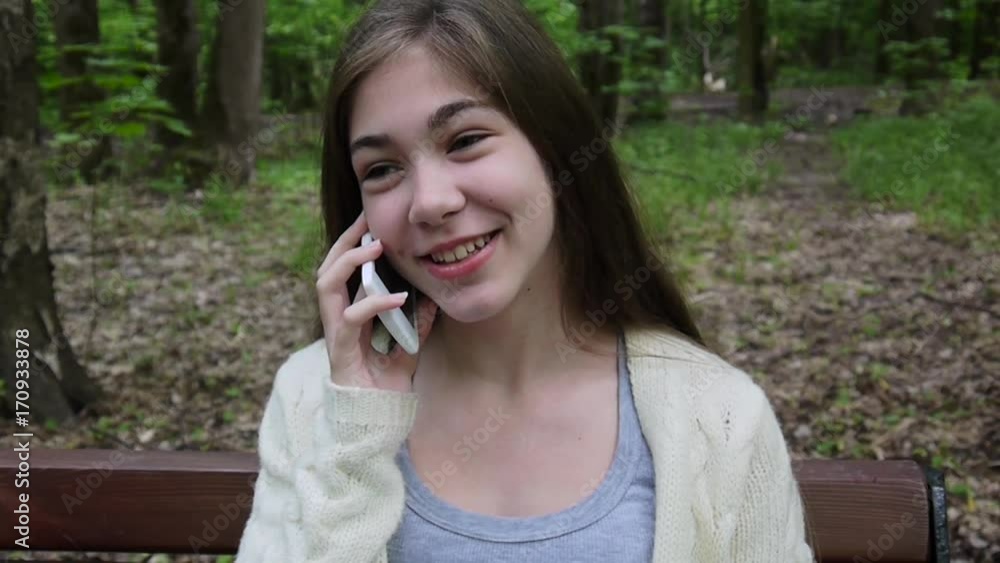 Young attractive girl speak to phone on bench. Summer park. Smile. HD video footage shooting static camera. Young attractive girl speak to phone on bench. Summer park. Smile. HD video footage shooting static camera.