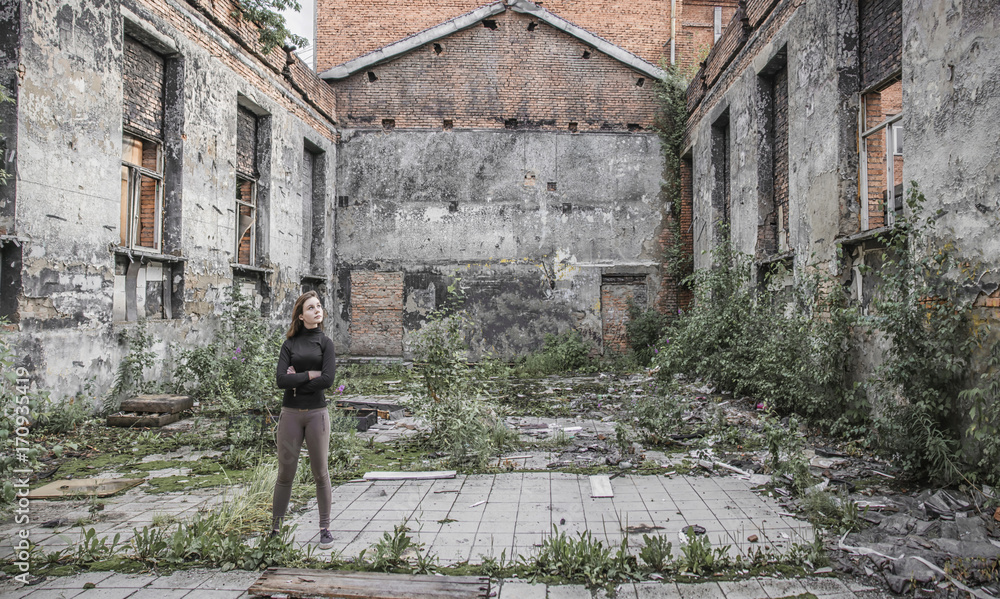 Wight girl standing in ruined abandoned building with trees growing inside