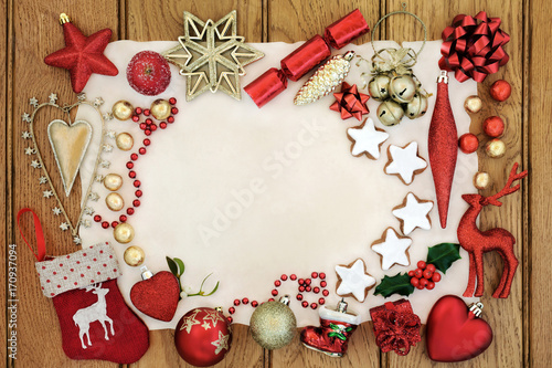 Christmas background border with bauble decorations, star shaped gingerbread biscuits, holly and mistletoe on parchment paper on oak wood.