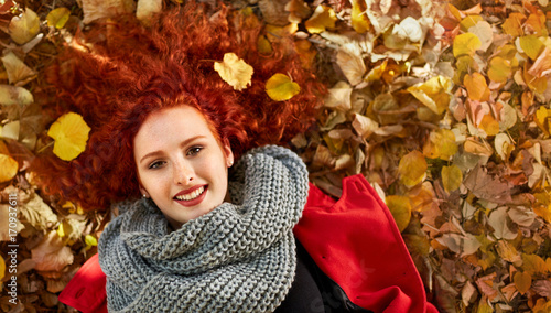 Ginger woman lying on leaves in park.