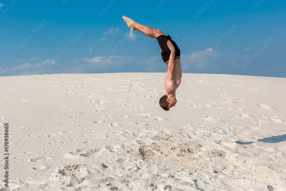 Portrait of young parkour man doing flip or somersault on the sand. Portrait of young parkour man doing flip or somersault on the sand.