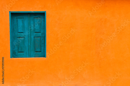Vivid bright orange colour facade with blue-green window and large empty orange wall texture background space.