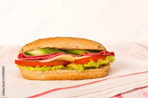 Sandwich with cheese, tomato, salami, cucumber and lettuce on wooden table