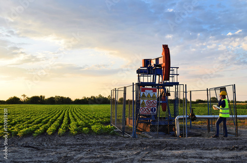 A female engineer at work on an European oil well during dusk time, agriculture field in background    