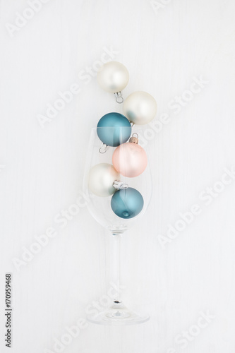 Multicolored Christmas balls in a champagne glass on a white. Minimalistic New Year's composition.