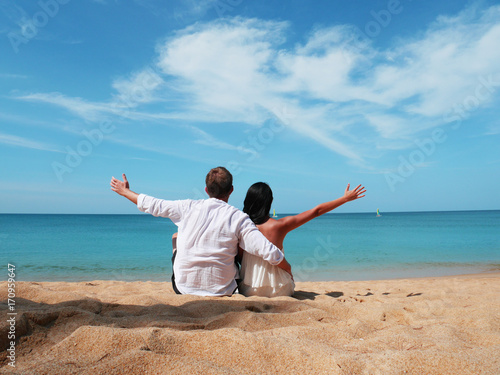 A happy couple in white sitting together looking a beach