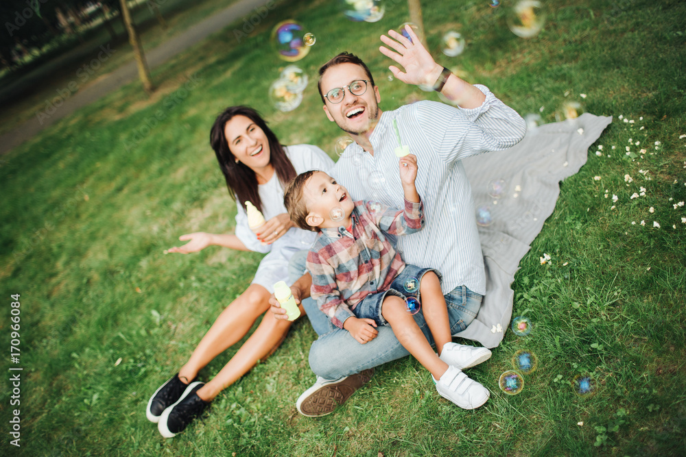Obraz premium Happy young family playing with bubble wands in park outdoors