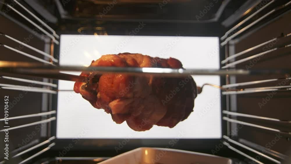 Cooking rotisserie roast pork neck in hot convection oven. Closeup of raw pork meat on a spit roasting under a grill element. View from inside of the electric cooker. Cooking rotisserie roast pork neck in hot convection oven. Closeup of raw pork meat on a spit roasting under a grill element. View from inside of the electric cooker.