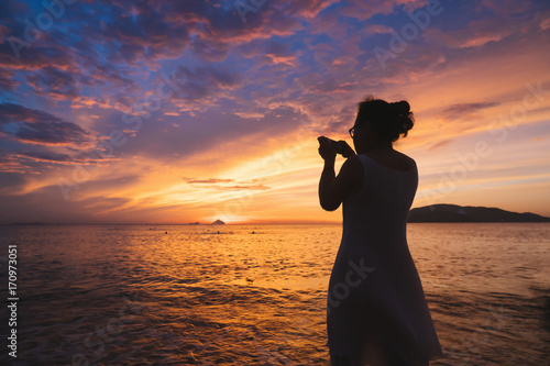 Woman make photo of beautiful sunrise over the ocean on smartphone.
