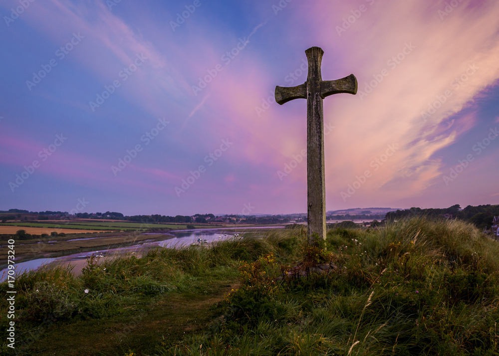 The Wooden Cross on Church Hill, Alnmouth, Northumberland, England. UK. The hill is the site of the long ruined church of St Waleric. At sunrise/ dawn with a colourful dawn sky.