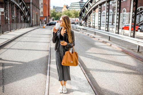 Lifestyle portrait of a stylish business woman standing with coffee cup outdoors on the old iron bridge