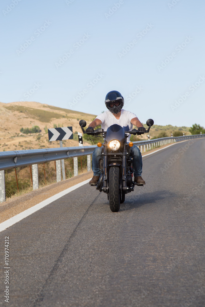 Obraz premium Young man riding a motorcycle on road in mountains in sunny day. 