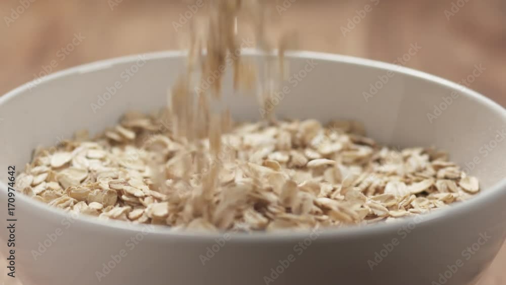 Slow motion closeup oat flakes falling into white bowl Slow motion closeup oat flakes falling into white bowl