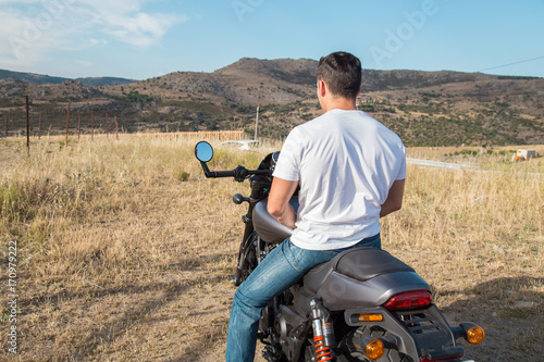 Back view of biker without helmet sitting on motorcycle in a mountain area.   