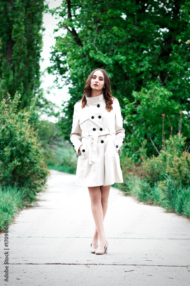 A woman or girl in a coat is standing on a quay among trees A woman or girl in a coat is standing on a quay among trees