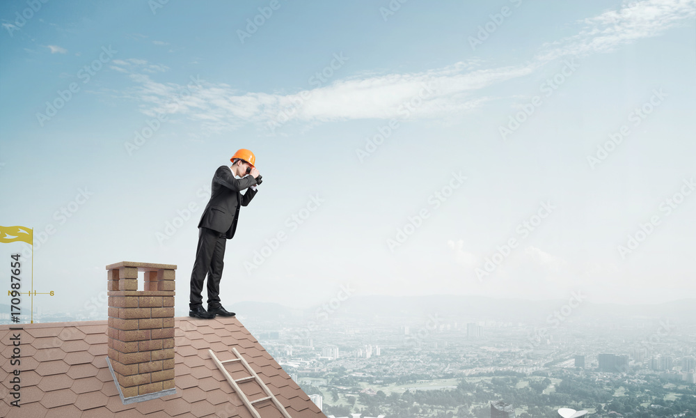 Engineer man standing on roof and looking in binoculars. Mixed media Engineer man standing on roof and looking in binoculars. Mixed media