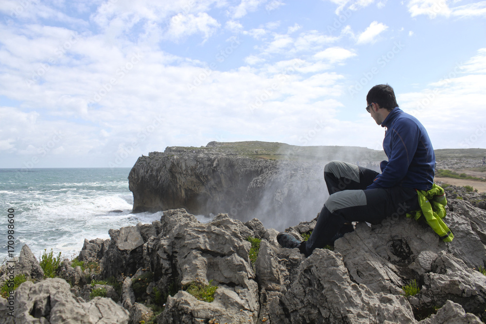 guy looking at the waves splashing against the rocks