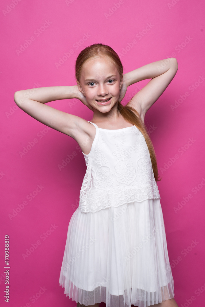 Beautiful little redhead girl in white dress posing like model on pink background. Beautiful little redhead girl in white dress posing like model on pink background.