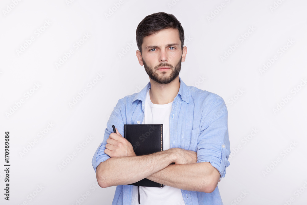 Headshot of attractive serious European student with beard, mustache, dressed in casual t-shirt, looking at camera with indifferent stony facial expression, keeping his arms folded white studio wall Headshot of attractive serious European student with beard, mustache, dressed in casual t-shirt, looking at camera with indifferent stony facial expression, keeping his arms folded white studio wall