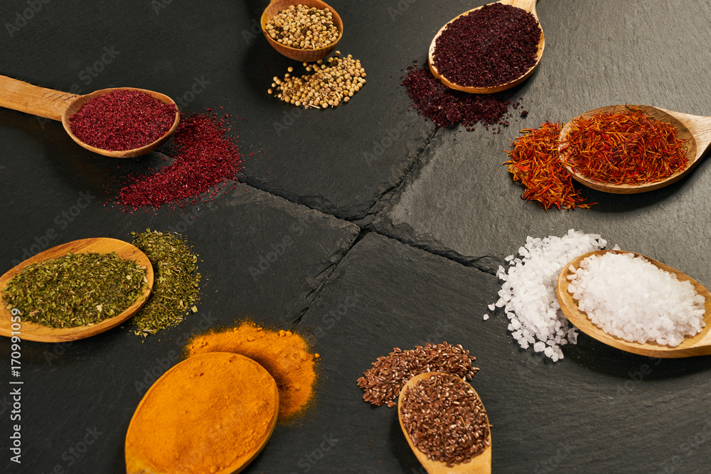 Colorful indian spices in wooden spoons on black stone background