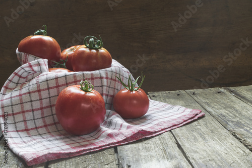 Group of tomatoes in basket with dishcloth on wooden table