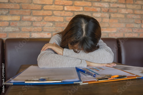 Frustrated female sleeping on many sales reports photo