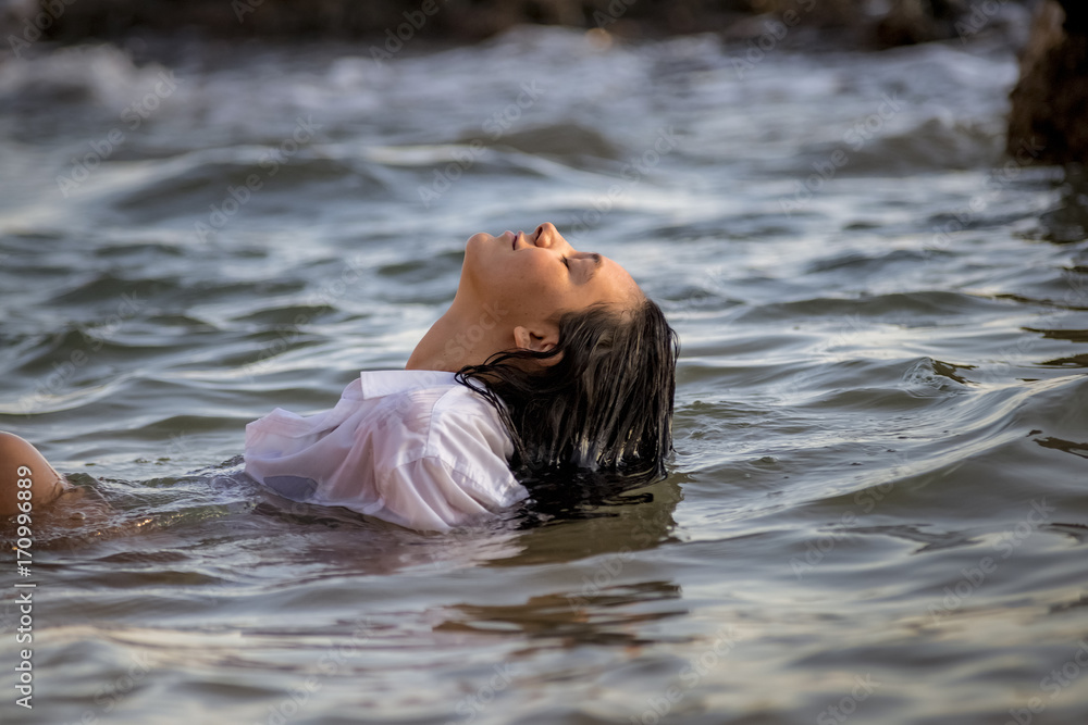 Fototapeta premium Chica joven con camisa blanca tumbada en el agua del mar al atardecer.