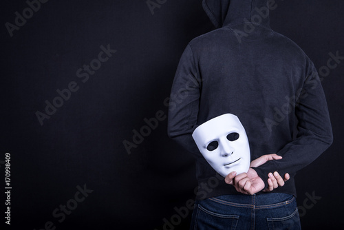 Mystery man holding white mask in the back. Anonymous social masking concept. photo