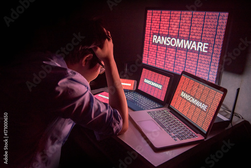 Young Asian male frustrated, confused and headache by ransomware attack on desktop screen, notebook and smartphone, cyber attack and internet security concepts photo