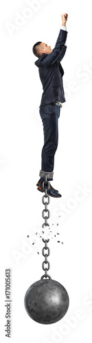 A businessman jumps in the air while connected to a large iron ball with a broken chain.