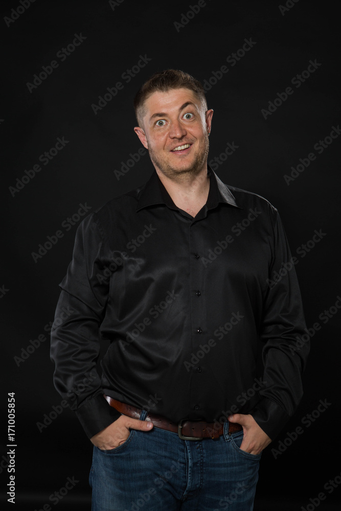 Young surprised man portrait of a confident businessman showing by hands on a black background. Ideal for banners, registration forms, presentation, landings, presenting concept.