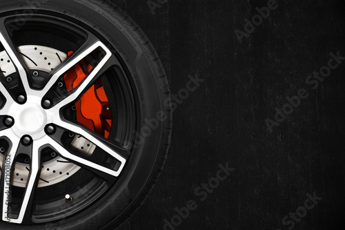 Alloy wheels of racing car with metal brake discs and red caliper on a black cement wall background with copy space your writing text on the right. Automotive parts concept. photo
