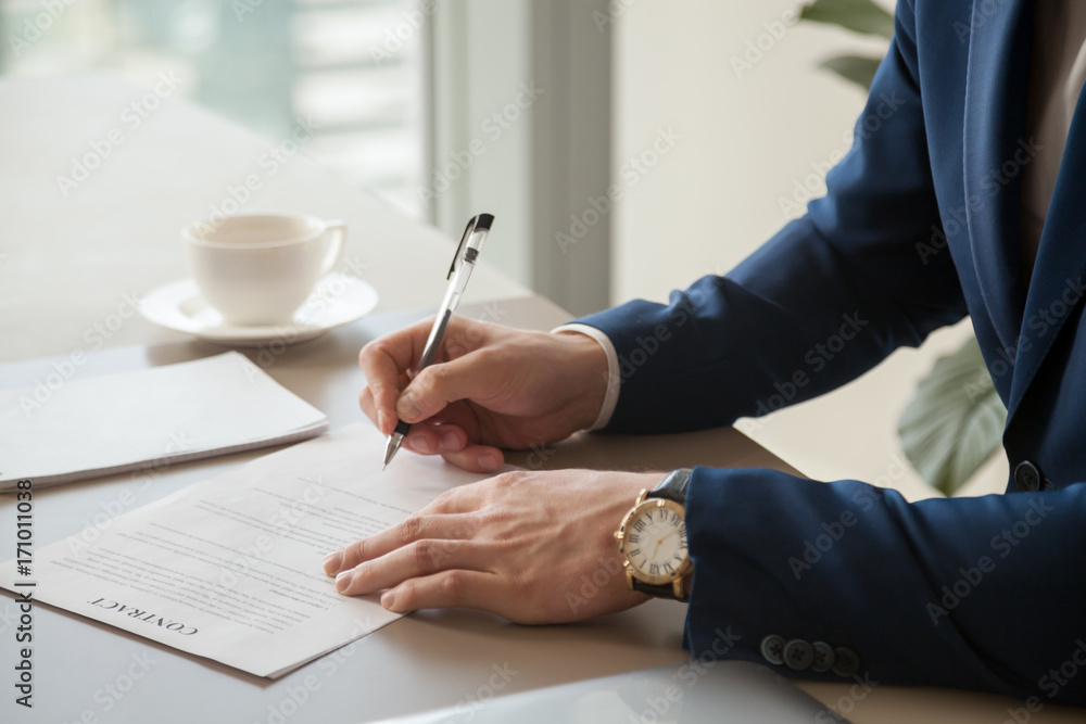 Φωτογραφία Businessman in blue business suit and expensive watch on hand putting signature on contract lying on desk