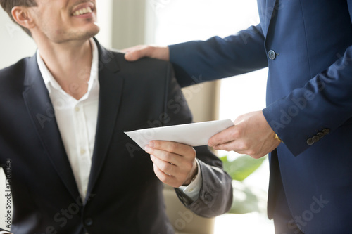 Company leader giving money bonus in paper envelope to happy smiling office worker, congratulating employee with increasing of salary or promotion, thanking for successes in work. Close up concept photo