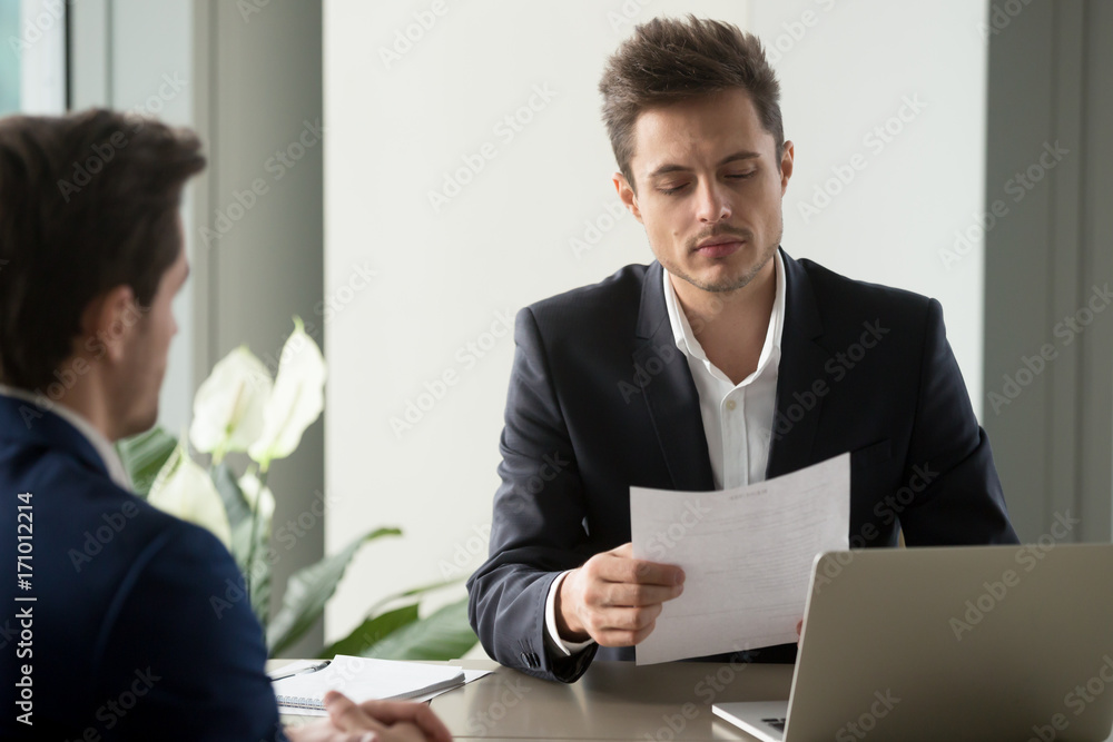 Φωτογραφία Company leader reading contract, attentively studying text of agreement, doubting some deal conditions while sitting at desk with business partner